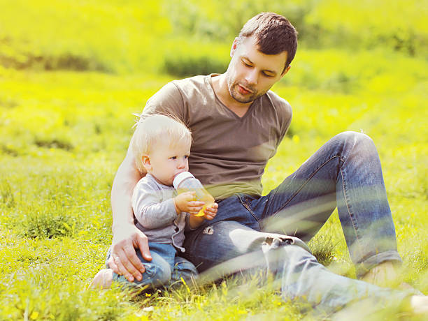 istock Father and baby drinks from a bottle sitting on grass 537396738
