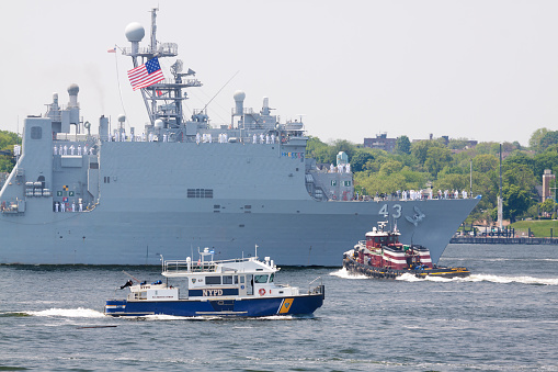New York, NY, USA - May 25, 2016: NYC Fleet Week 2016, dock landing ship USS Fort McHenry (LSD 43) in New York Harbor. NYPD boat, Tug Boat, American flag, bay water and green trees of Staten Island are in the image. Canon EF 70-200mm f/4L IS lens.