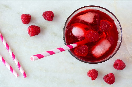 Raspberry fruit drink in a glass with straw, overhead view on a white marble background