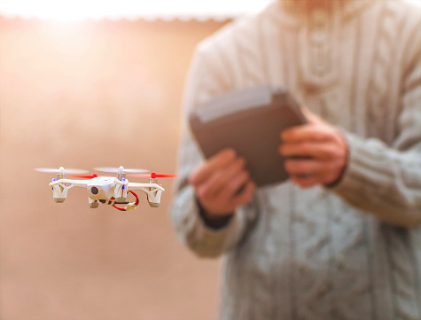 Paris, France - January 3, 2015: Hubsan FPV X4, small quadricopter drone flying in selective focus with unrecognizable man in background. It's the world's smallest FPV (first person view) quadcopter. The toy has a front camera to see the captured image directly on the remote control. 2.4GHz RC series, 480p camera and 4.3 inch LCD. Hubsan is a leader in flying object model.