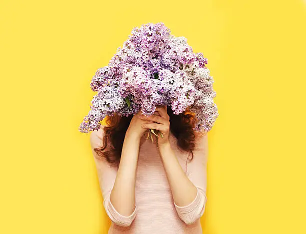 Photo of Woman hiding head in bouquet lilac flowers over yellow background