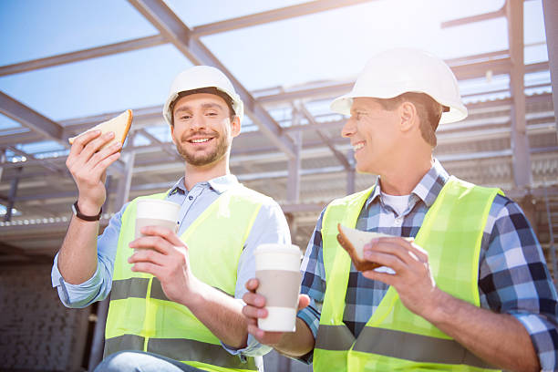 Modern building business and workers Lunch-hour.  Smiling and very positive workers having meal break and holding cups of nice coffee and tasty sandwiches while being on construction  construction lunch break stock pictures, royalty-free photos & images