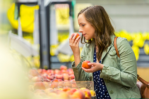 Young Vietnamese woman smelling ripe apple in supermarket