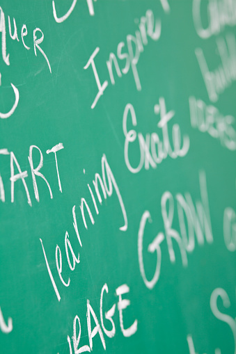 A variety of encouraging and motivational words are written in chalk on a traditional green chalkboard in school classroom.