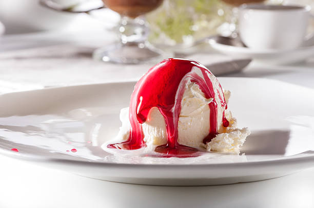 ice cream scoop with berry syrup on white plate close-up
