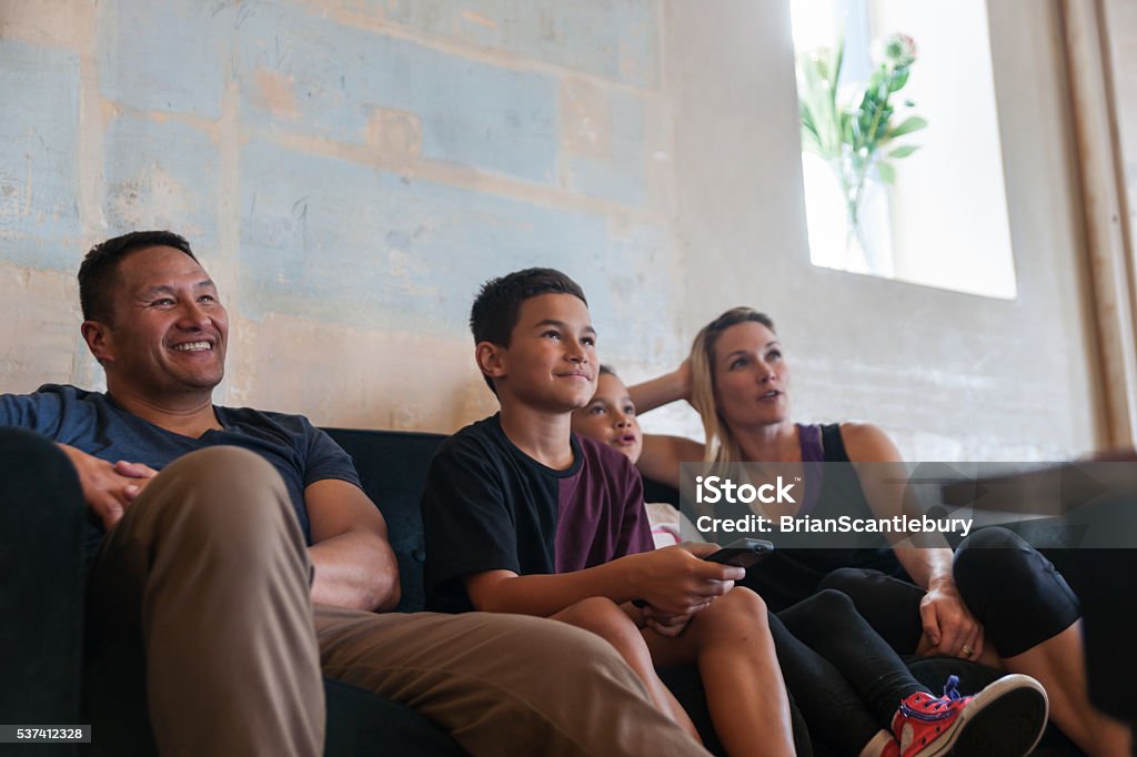 Family sitting together in lounge Modern nuclear family in soft focus of racial diversity happily sitting together in lounge looking in same direction focus on children. Family Stock Photo