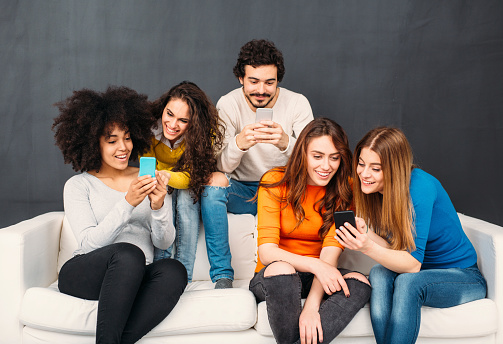 Five friends sitting on a couch in front of a blackboard and browsing the internet.