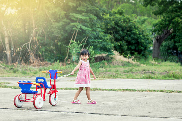 Child cute little girl having fun to pull her tricycle and walking in the park,vintage color filter