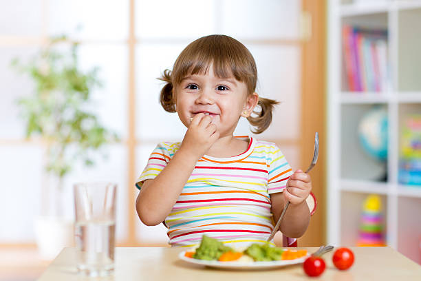istock Happy child girl eats vegetables sitting at table in nursery 537422754