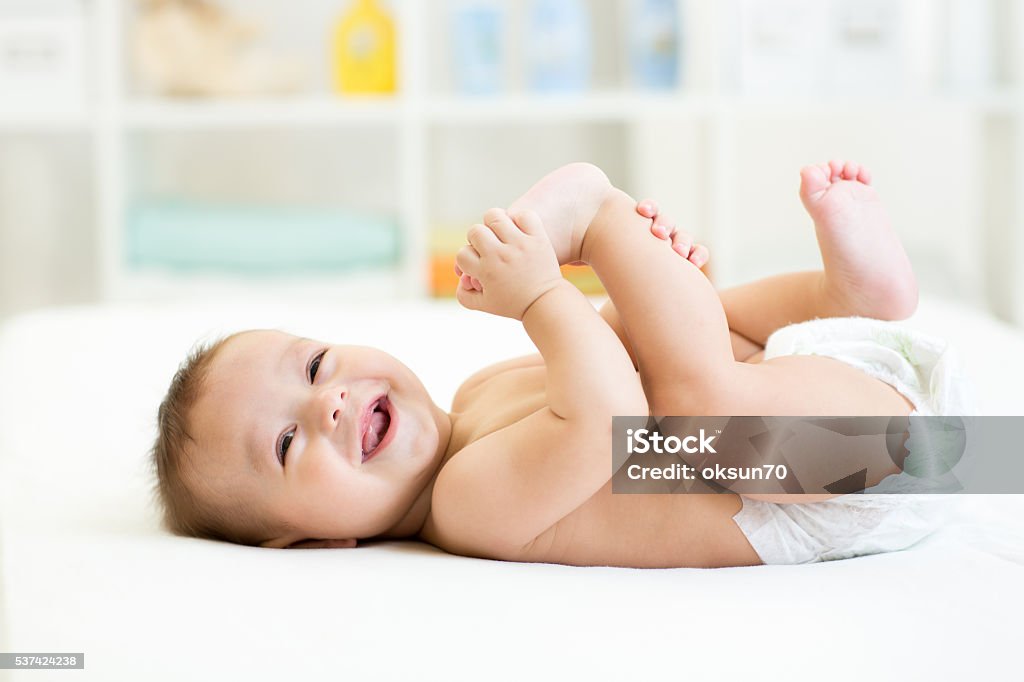 baby lying on white bed and holding legs baby lying on white sheet and holding his legs Baby - Human Age Stock Photo