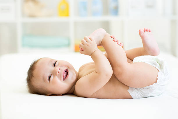 baby lying on white bed and holding legs baby lying on white sheet and holding his legs Diaper stock pictures, royalty-free photos & images