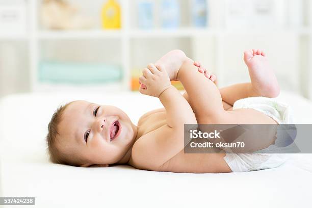 Baby Lying On White Bed And Holding Legs Stock Photo - Download Image Now - Baby - Human Age, Diaper, Smiling