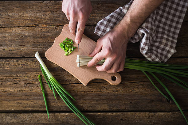man chopped green onion on the board. Wooden table