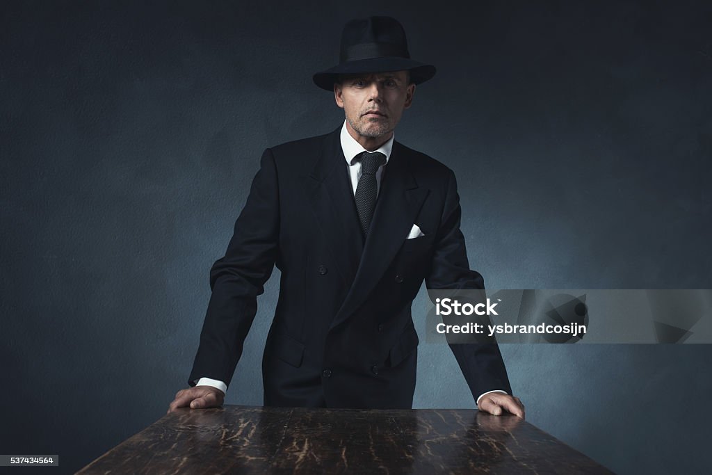 Bossy vintage 1940 businessman standing behind wooden table. Gangster Stock Photo