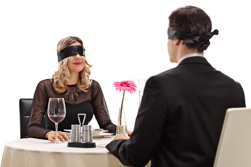 Young man and woman sitting on a blind date at a restaurant isolated on white background