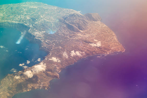 Greek Island Santorini in Aegean sea, aerial view from flight altitude of aircraft. Sun reflected from the water surface through the clouds. Front blurred background with bokeh