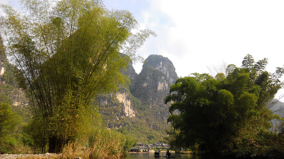 Yangshuo, Gulin, China - December 27th, 2015: peculiar karstic mountains and hills landscape along the bamboo banks of Yangshuo River, frecuently crossed by bamboo rafts, in the south of China.