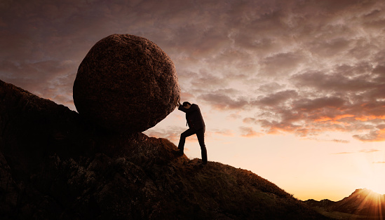 Silhouette of young businessman pushing large stone uphill with copy space