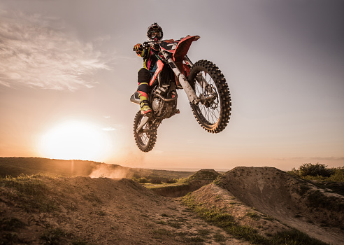 Low angle view of Enduro motocross rider jumping high up off-road at sunset. Copy space.