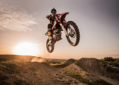 Motocross rider performing high jump at sunset.