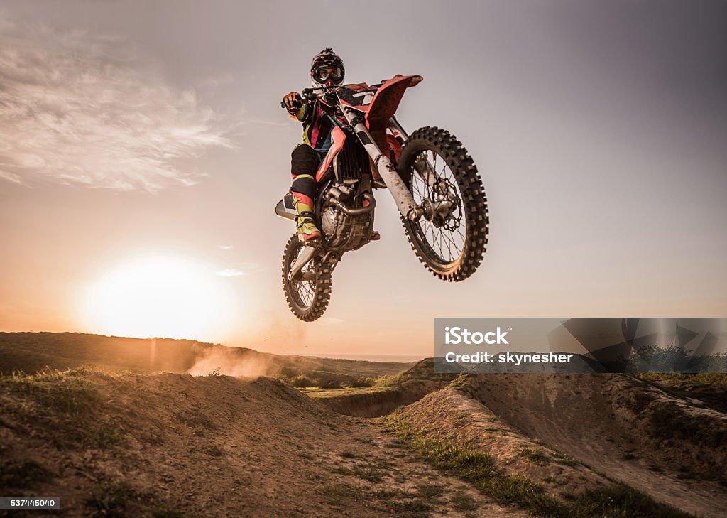 Motocross rider performing high jump at sunset. Low angle view of Enduro motocross rider jumping high up off-road at sunset. Copy space. Motocross Stock Photo