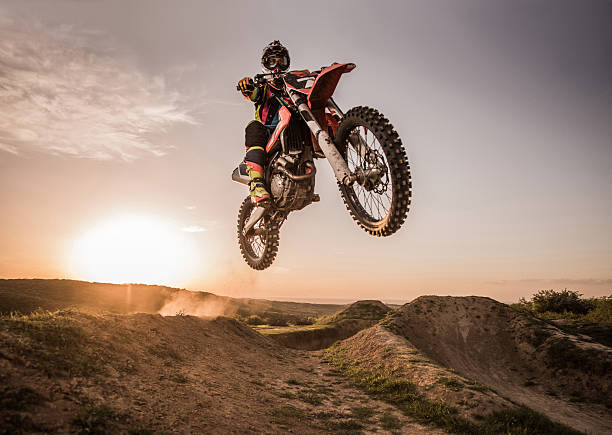 Motocross rider performing high jump at sunset. Low angle view of Enduro motocross rider jumping high up off-road at sunset. Copy space. dirt road sunset stock pictures, royalty-free photos & images