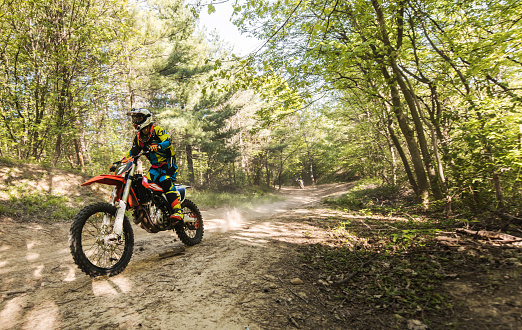 Motorcyclist riding motocross dirt bike on a single lane road in the forest.