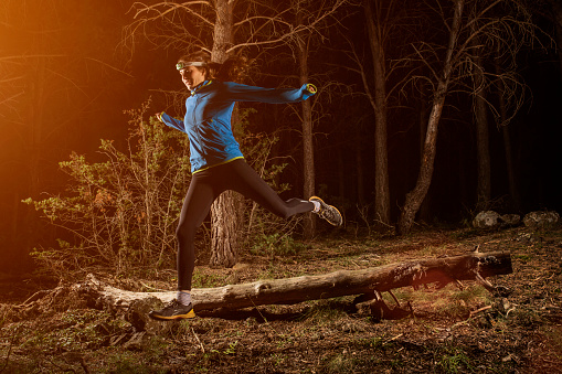 Full length of young female jogger running in forest at night