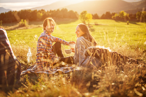 Happy young couple holding bowls while relaxing on field