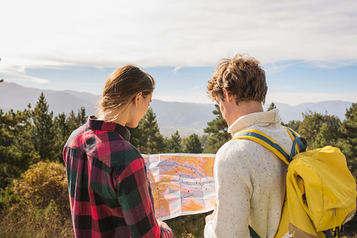 Rear view of hiking couple reading map with trees and mountains in background