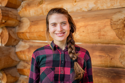 Portrait of happy young woman standing against log cabin