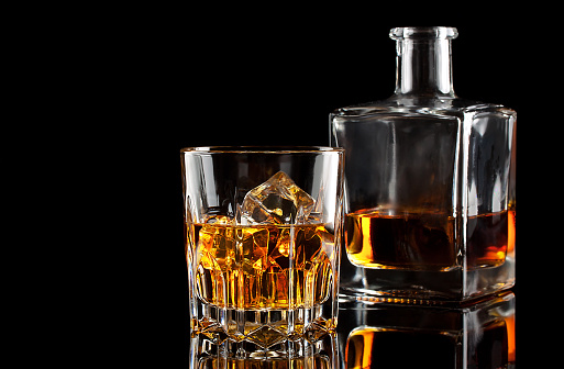 Glass of whiskey with ice and a square decanter isolated on a black background