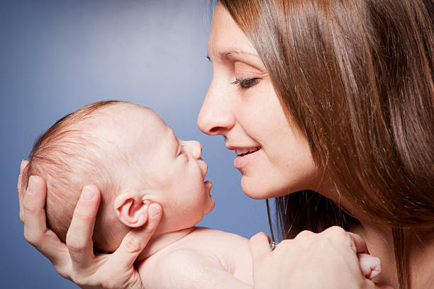A smiling mother and her smiling one month old baby boy smiling as they look into each other's eyes.