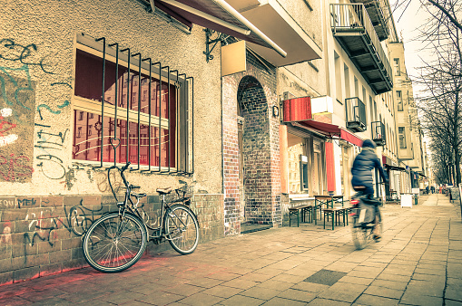 Vintage retro travel postcard of a narrow street in the former east side of Berlin - Mix of past and present in the multicultural capital fo Germany - Everyday life with people and bike on the road