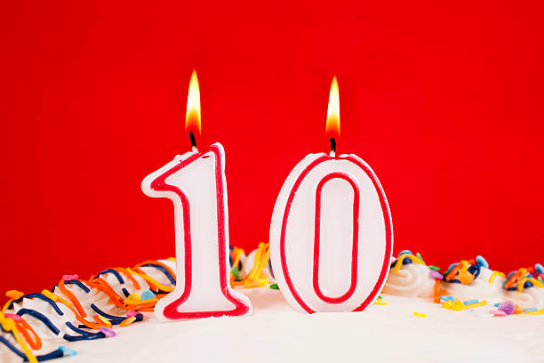 istock Decorated birthday cake with number 10 lit candles.  Red background. 537456853