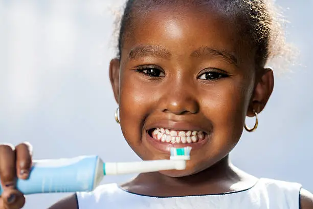 Close up portrait of cute little afro girl holding electric toothbrush ready to brush teeth.