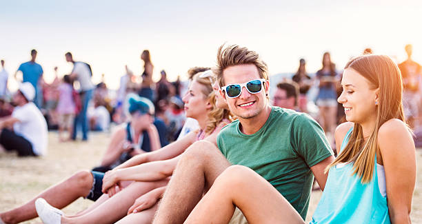 Teenagers at summer music festival, sitting on the ground Teenage boy and girl enjoying a summer music festival with their friends, sitting on the ground teenager couple child blond hair stock pictures, royalty-free photos & images