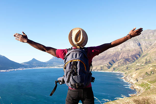 Young man on holiday standing with arms spread open Rear view portrait of young man with backpack standing on a mountain with arms spread open vista posterior stock pictures, royalty-free photos & images