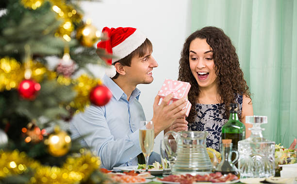 Couple giving presents at Christmas dinner Smiling man giving present to happy girlfriend during romantic Christmas dinner with champagne in home wonderingly stock pictures, royalty-free photos & images