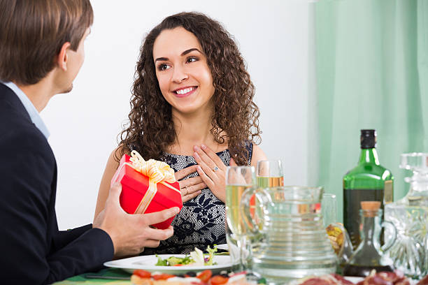 Man giving present to woman during dinner Man giving present to woman during romantic dinner in home wonderingly stock pictures, royalty-free photos & images