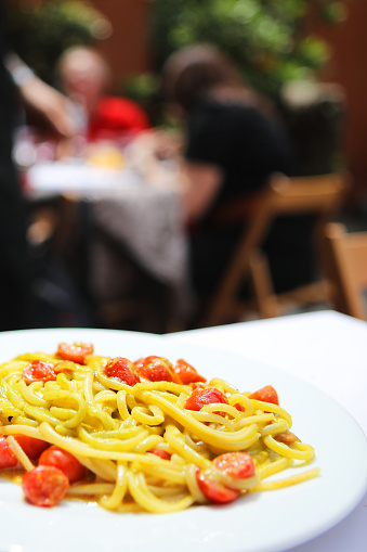 This is a vertical close-up image of Italian tonnarelli pasta with fresh cherry tomatoes served on a plate at an outdoor restaurant in Trastevere in Rome Italy. Blur background provides plenty of space for text.