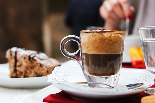 Italian coffee Caffè Marocchino served with a small glass of water at a restaurant in Rome. A slice of homemade Italian cake is seen in the background.