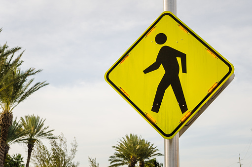 Photo of a yellow pedestrian crossing sign with flashing lights against cloudy sky
