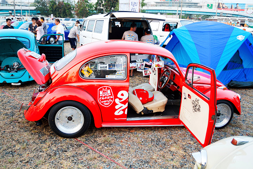 Bangkok, Thailand - February 15, 2014: Capture of many VW oldtimers on Siam VW festival and public meeting, In foreground is a red restored VW Beetle. Car is decorated with many photos. In background are many more cars and Thai people watching cars or talking to owners.