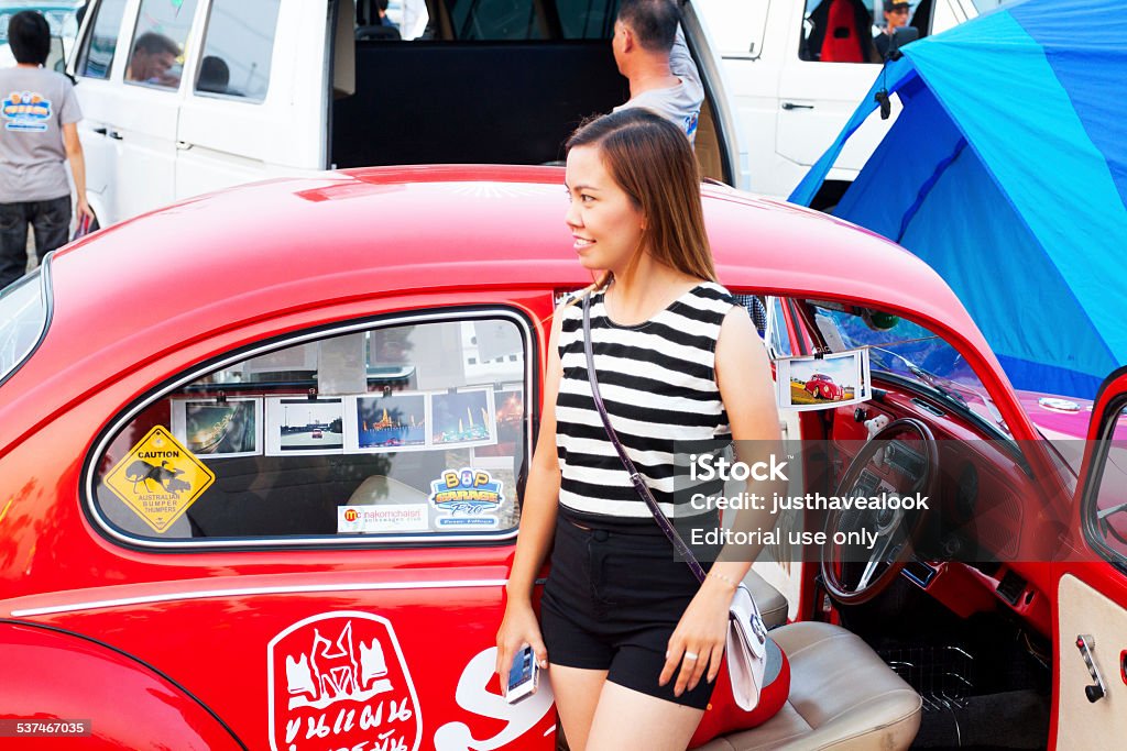 Photo with red VW Beetle oldtimer Bangkok, Thailand - February 15, 2014: A Thai woman is posing for a photo with a fine restored red VW Beetle oldtimer. Oldtimer is decorated with many photos. In background are more people at a VW van oldtimer. Scene is on Siam VW festival in Bangkok. 2015 Stock Photo