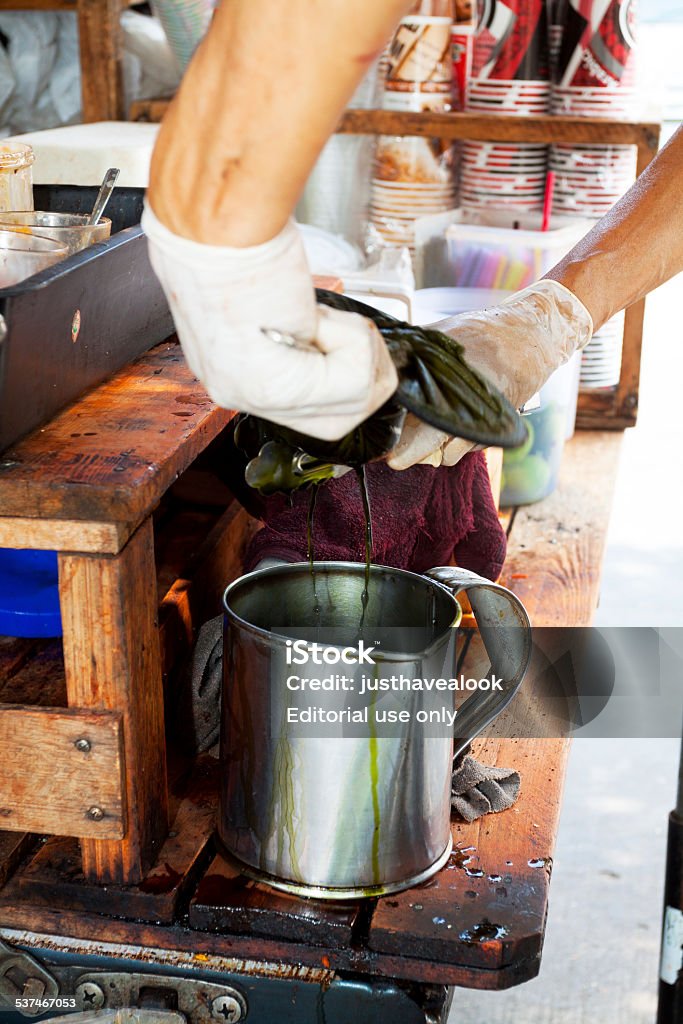 Wringing tea sieve at street market stall Bangkok, Thailand - February 8, 2014: Capture of hands of Thai man wringing tea sieve and filter. Scene is at a street coffee and tea shop and market stall. In background are many cups. Man is wearing gloves. 2015 Stock Photo