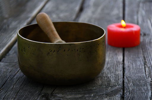 Singing Bowl and burning red candle on a wooden background