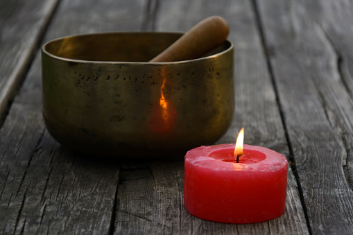 Singing Bowl and burning red candle on a wooden background