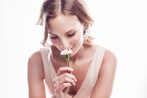 Beautiful young woman smelling  a flower with a look of love on her face.