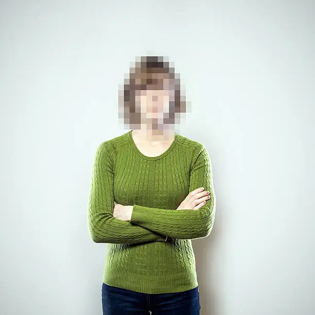 A portrait of a woman from the waist up, whose face has been rendered unrecognizable by being pixelated.  A conceptual representation of individual identity protection or harassment.  Square crop with copy space on a a clean off-white background.